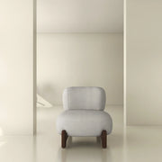 Modern minimalist armchair with light grey upholstery and wooden legs in a neutral interior space